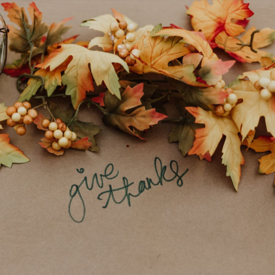 fall leaves on table next to phrase 'give thanks'